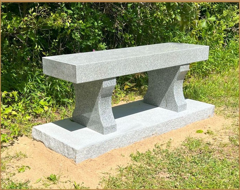 A plain granite memorial bench standing on a lawn