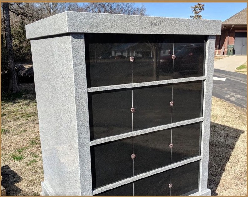 A tall grey granite columbarium with black niche fronts