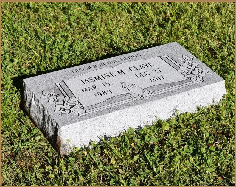 A flat grass level granite marker with carved detail, set flush in the grass