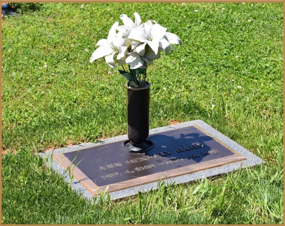 A flat granite marker with a black vase of white lilies set beside it