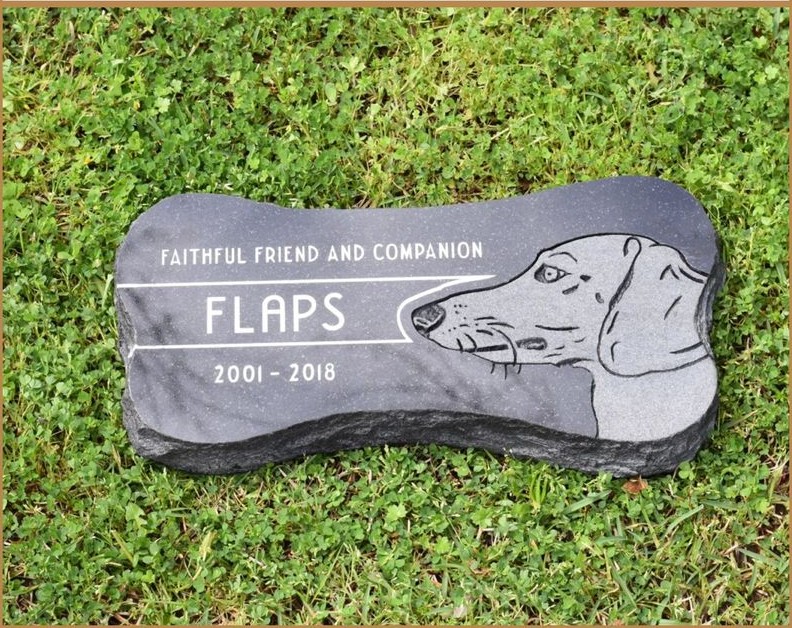 A granite pet marker carved with a portrait of a dog and the name FLAPS